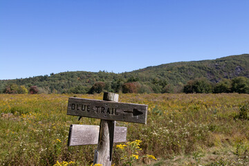 Trail sign pointing the direction.  Big blue sky, field and mountains in the background