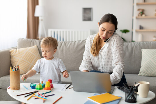 Mom balances work and parenting by taking calls and using her laptop while her child plays with colorful blocks on the table in a cozy living room. - Powered by Adobe