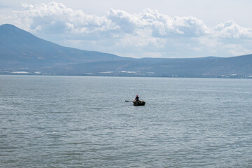 Solitary fisherman on wooden boat in the middle of Lake Chapala with distant mountains in view