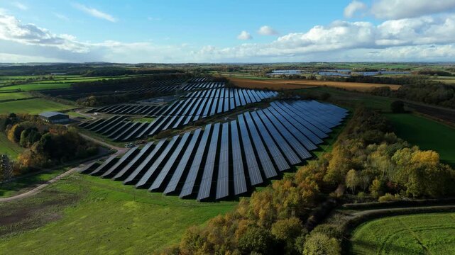 Drone flyover of utility solar field with maintenance tracks and inverter stations in a green landscape near Nottingham
