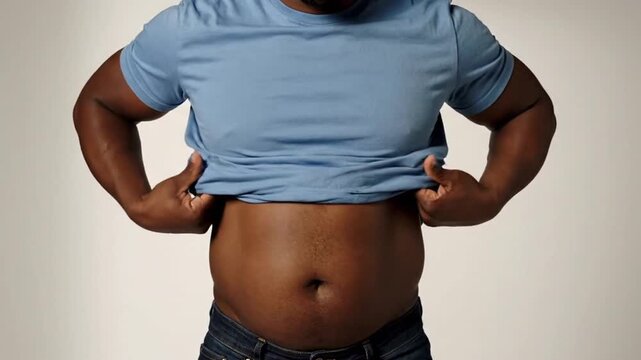 Dark Skinned Man in Blue T-Shirt Against a Neutral Background Revealing His Stomach with Strong Lighting. T-shirt Design Template for Adobe Stock Photos