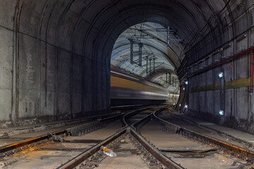 Obraz premium A train blurs through the dark, arched tunnel of Rossio Train Station, creating a sense of speed as it passes the track junction.