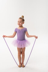 Little ballerina with cochlear implant holding jump rope in studio. Inclusive childhood, hearing technology, and confidence through rhythm, grace, and balance.