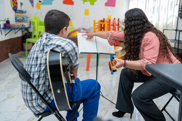 Music teacher pointing at the sheet music while giving instructions to a young boy during a private guitar lesson. One-on-one teaching, musical learning, chords, and instrumental education