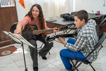 Music teacher guiding a young boy during a guitar lesson, pointing at the sheet music and explaining rhythm and chords. Private instruction, focused learning, and musical education in a calm environme