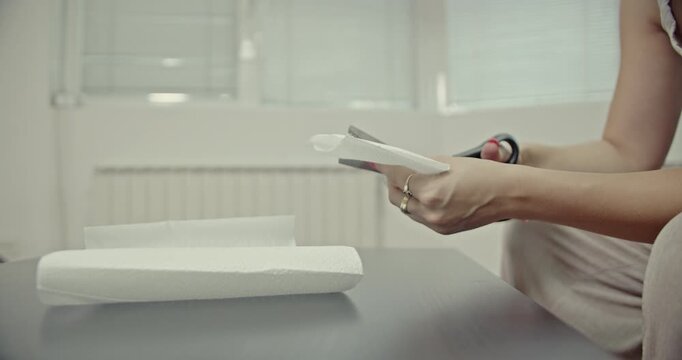 Close-up of a woman's hands cutting white paper with scissors, creating satisfying sound effects. This engaging clip highlights the simple yet precise actions of crafting and domestic activity.