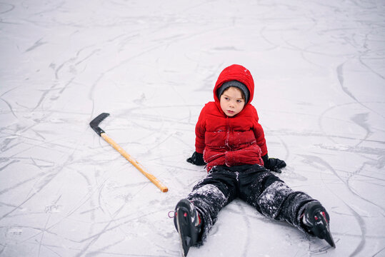 Young Boy in skiwear sitting on a frozen pond with his hockey stick