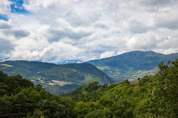 Fototapeta premium Green meadows and cloudy mountains on the road to La Salle-en-Beaumont in the Auvergne-Rhone-Alpes region, France