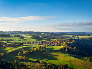 Rolling Bavarian hills in golden autumn, tranquil Morgenbach village and patchwork farms under vast blue sky, ideal for rural tourism ads.