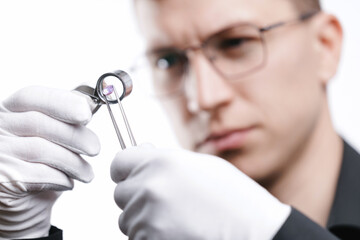 Male jeweler examining pink diamond with loupe and tweezers in professional setting, white studio background