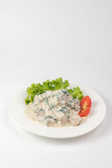 Creamy mushroom and spinach dish served on white plate with fresh greens a white background
