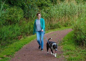 Young woman with glasses walking her black and white mixed breed dog along a path