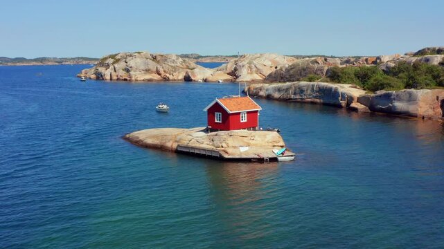 Fjord in Norway with small summer cottage fishing shed on single island big smooth rock or stone between islands ocean. Clear water natural environment. Boats and kayaks