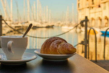 Croissant and coffee against the backdrop of the bay with yachts.