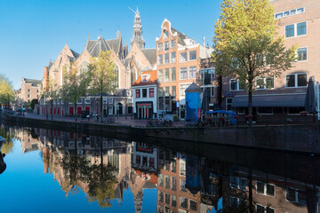 Facades of old historic Houses, cathedral church and trees over canal water, Amsterdam, Netherlands
