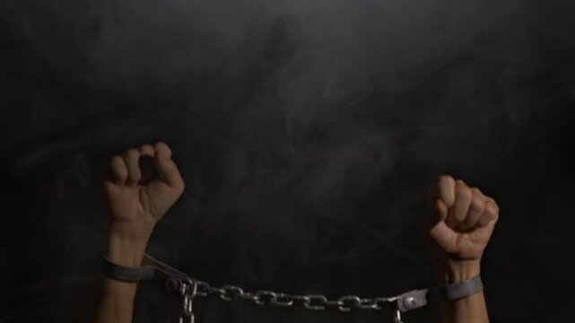 A man with hands bound in irons on a smoky black background