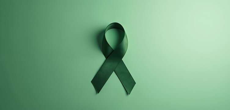 Green awareness ribbon lays on green background. Symbol of support for mental health, well-being. Concept of hope, prevention, campaign against disease. Table top view from above.