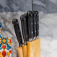 Close-up of kitchen knives with black handles neatly arranged in a wooden block on a marble countertop. Perfect for culinary, cooking, professional chef tools, and kitchen organization concepts