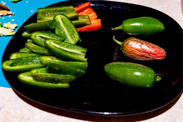 Fresh green and red jalapeño peppers, sliced and whole, arranged on a black plate. Concept of spicy food, freshness, and colorful culinary ingredients