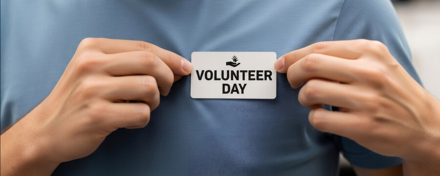 Man showing volunteer day badge on blue t-shirt for International Volunteer Day concept. Charitable organization support and community service awareness.
