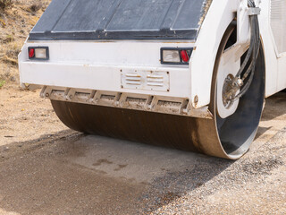 Road roller machine or compactor, working on fresh loose gravel, pressing and leveling material for new roadbed. Heavy construction equipment