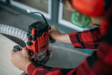 A young man is working with a milling cutter on the veranda of a house. Close-up of hands holding the machine. The carpenter is chamfering plywood using the milling machine.