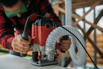 A young man is working with a milling cutter on the veranda of a house. Close-up of hands holding the machine. The carpenter is chamfering plywood using the milling machine.