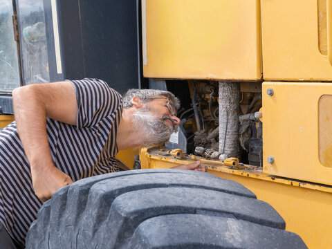 hispanic Man with beard and glasses performing inspection on heavy machinery engine. Worker checking equipment reliability at construction site