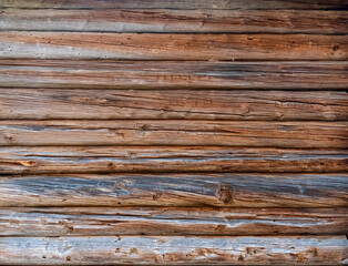 Obraz premium close-up view of a wall constructed from weathered, horizontal wooden logs. variety of textures and natural color variations, with some appearing aged and greyed, while others retain a warm brown hue.