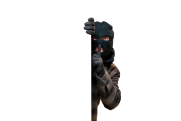 Thief wearing a black balaclava peering from behind a white blank sign, signaling silence with a finger over lips