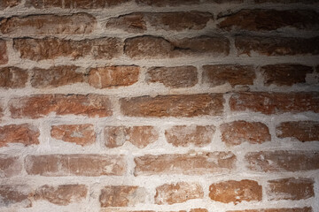 Darkened red brick wall with soft shadows and warm tones, creating a vintage rustic background ideal for design, architecture, or interior atmosphere concepts