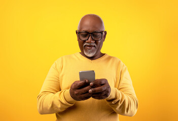 Senior black man smiles as he uses his smartphone to chat with a friend. The scene features an...