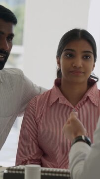 Vertical video young indian couple listening intently to male doctor during medical consultation in bright clinic, concerned but hopeful