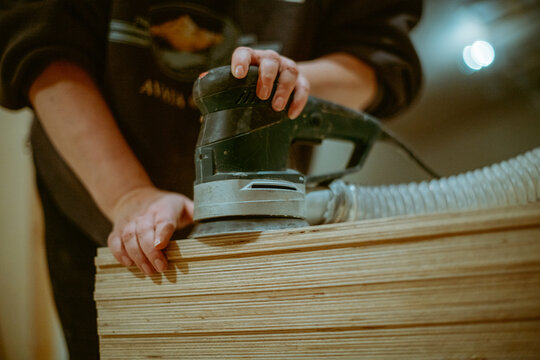 A young woman grinds plywood in a house under construction. Close-up of a woman's hands holding a grinder. A woman works with a manual electric grinder