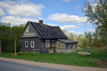 Fototapeta premium Old wooden time-worn house in Russia village with a slanted roof surrounded by green grass on a sunny day. Concept of villages in the Russian outback