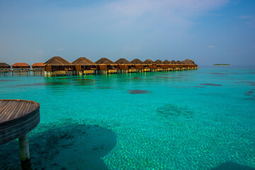 Tranquil closeup calm sea water waves with palm trees. Bungalows background. Tropical island beach landscape exotic shore coast. Summer vacation, holiday amazing nature. Relax paradise, Maldives.