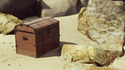 A wooden treasure chest sits on a sunlit sandy beach, framed by smooth rocks. The scene captures a moment of calmness and adventure, inviting curiosity and exploration.