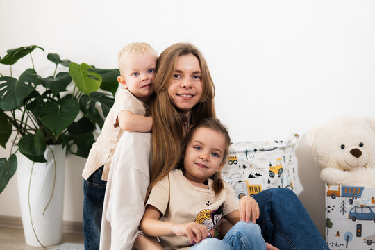A happy mother with children at home is family happiness and care. A warm family scene of a blonde haired girl and two children sitting on the floor in a cozy room