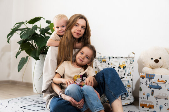 A happy mother with children at home is family happiness and care. A warm family scene of a blonde haired girl and two children sitting on the floor in a cozy room