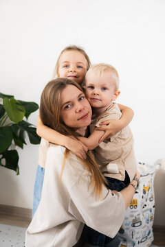 A happy mother with children at home is family happiness and care. A warm family scene of a blonde haired girl and two children sitting on the floor in a cozy room