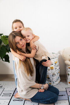 A happy mother with children at home is family happiness and care. A warm family scene of a blonde haired girl and two children sitting on the floor in a cozy room