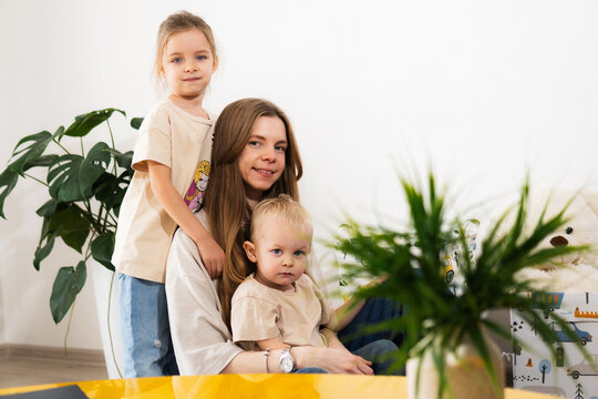 A happy mother with children at home is family happiness and care. A warm family scene of a blonde haired girl and two children sitting on the floor in a cozy room