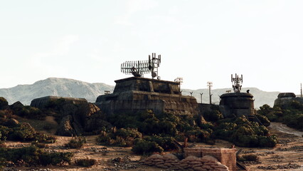 Obraz premium Abandoned telecommunications towers rise above a barren landscape, surrounded by rocky mountains and sparse vegetation under a clear sky during daylight.