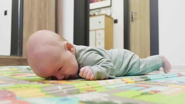 newborn baby boy lying on belly and trying to hold his head. Two month old infant have tummy time. The baby trains the back muscles by lifting head. Exercise for developing motor skills