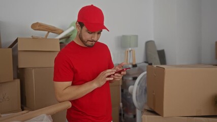 Man in red cap taps smartphone screen with finger inside building surrounded by moving boxes; efficiency.