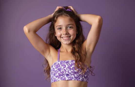 Young girl wearing purple, white bikini top. Long brown hair, smiling. Girl posing with hands on head, looking confident, carefree. Ready for summer vacation fun day at beach pool.