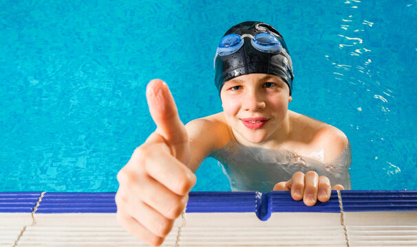Preteen boy swimming in indoor pool during swim class and showing thumb up
