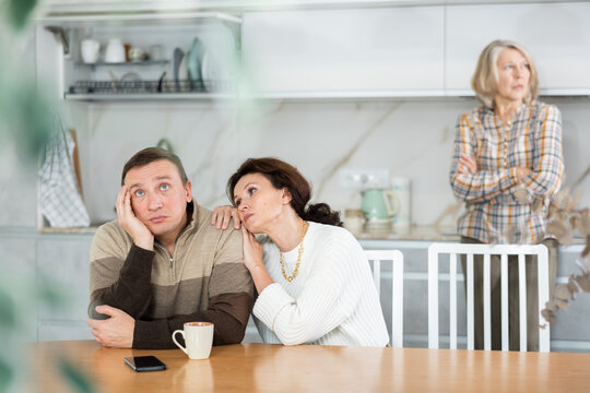 Kind woman asking livid middle-aged man for forgiveness during domestic quarrel in the kitchen