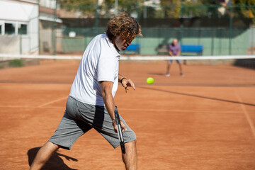 Back view of active male player hitting ball with racket on indoor tennis court on blurred background of opponents