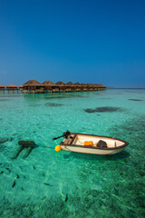 Fototapeta premium Tranquil closeup calm sea water waves with palm trees. Boat and bungalows background. Tropical island beach landscape exotic shore coast. Summer vacation, holiday amazing nature, Maldives.
